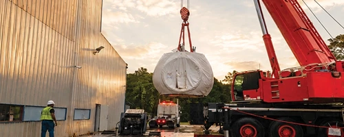 Mobile crane lifting wrapped heavy equipment during a specialized logistics operation.