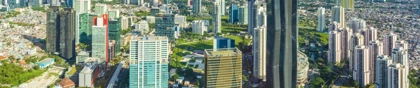 Panoramic aerial view of Jakarta's modern skyline with skyscrapers, green spaces, and urban infrastructure under a clear sky