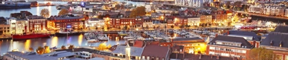 Evening aerial view of Dunkirk, France, featuring illuminated harbor, boats, and city buildings